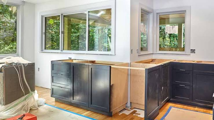 Kitchen renovation in progress with dark cabinets, unfinished wooden countertops, large windows and protective coverings on the floor